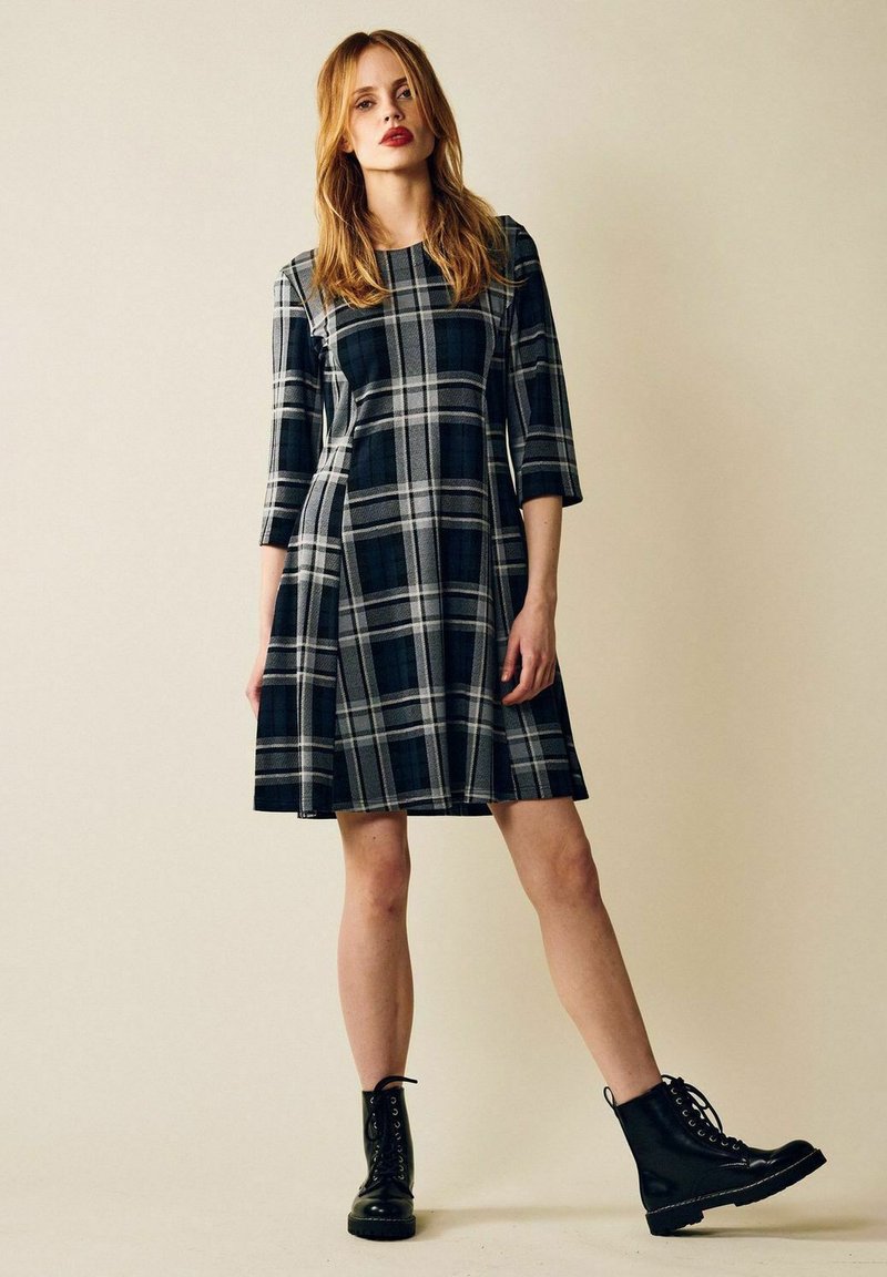 Mustat ja harmaat ruudulliset mekot, joissa on kolmanneksen hihat, A-linjainen muotoilu, polvimittaiset, yhdistetty mustiin nauhakenkiin.