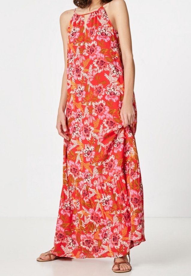 Robe maxi en rouge vif avec de grands motifs floraux roses. Présente un design à col halter et une coupe fluide et ample. Portée avec des sandales plates.