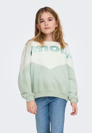 Zelen in bel pulover z vzorcem gora, na prsih bleščeč napis "mout" ter rebrasti manšeti in rob.