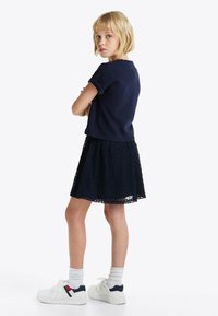 Top de manga corta azul marino combinado con una falda de encaje azul marino. Zapatillas blancas con acentos en azul y rojo. Calcetines ligeramente por encima del tobillo.