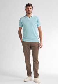 Polo shirt azzurro chiaro con maniche corte e colletto bianco, abbinato a pantaloni beige e sneakers bianche, indossato da un modello maschile in piedi.