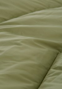 Ropa de cama verde oliva con una superficie suave y ligeramente brillante, que presenta suaves pliegues y costuras que destacan el diseño acolchado.