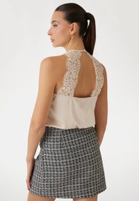 Top cu spate din dantelă în crem, cu un design în formă de cheiță, asortat cu o fustă mini din tweed alb-negru, cu un model texturat.
