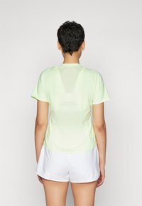Camiseta atlética de manga corta color verde claro con un panel de malla en la parte posterior, combinada con pantalones cortos blancos. Textura suave y diseño ajustado.