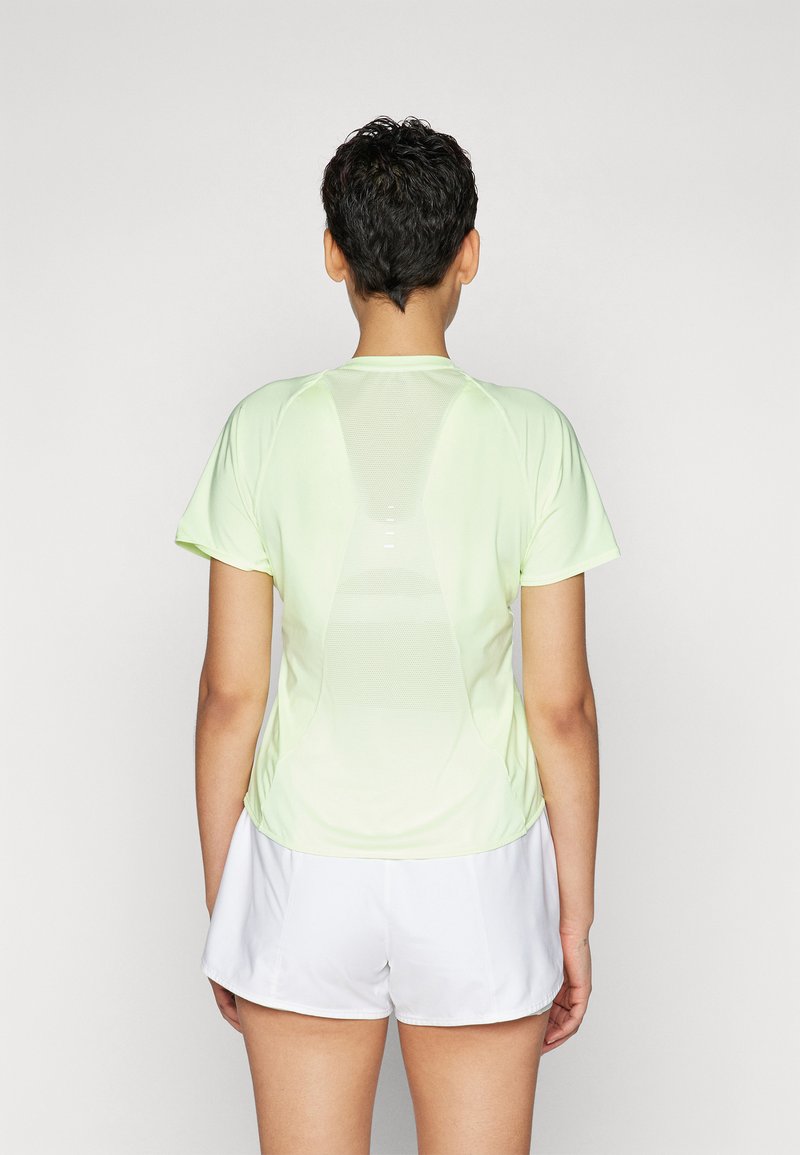 Kurzärmliges, hellgrünes Sportshirt mit einem Netzpanel auf dem Rücken, kombiniert mit weißen Shorts. Glatte Textur und figurnaher Schnitt.