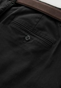 Sorte bukser med en glat tekstur, som har en knapdetalje på baglommen og et brunt læderbælte placeret ovenfor.