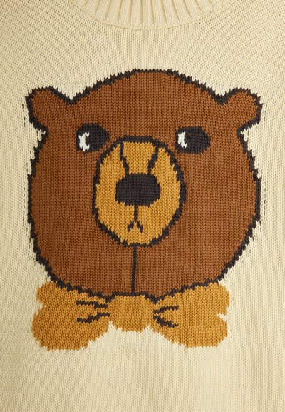 Suéter de punto con base crema, que presenta un gran diseño de oso marrón con un lazo amarillo, puntos texturizados y acentos en negro contrastantes.