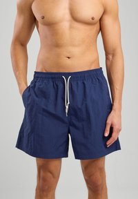 Shorts de bain navy avec une taille élastique à cordon de serrage ; fabriqués en tissu léger, comportant des poches latérales et une surface unie et texturée.