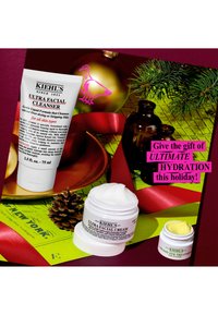 Kiehl’s Ultra Facial Cleanser, Cream, and Eye Treatment with holiday decor, pinecone, red ribbon, and text promoting ultimate hydration gift.
