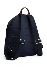 Σκούρο μπλε καπιτονέ σακίδιο με καφέ δερμάτινες λεπτομέρειες, επενδεδυμένους ιμάντες και χρυσά μεταλλικά εξαρτήματα. Διαθέτει στρογγυλεμένο σχήμα και ανθεκτικές ραφές.