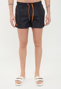 Pantaloni da bagno neri realizzati in materiale leggero, con vita elastica e lacci arancioni a contrasto, dettagli laterali e logo.