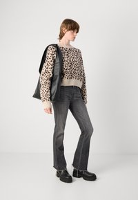 Leopardenmuster Strickpullover mit gerippten Bündchen und Saum, kombiniert mit ausgewaschenen grauen Schlagjeans und klobigen schwarzen Plateaustiefeln, außerdem wird eine schwarze Tasche getragen.