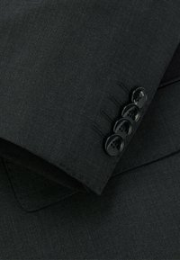 Giacca nera in tessuto con una texture liscia, dotata di quattro bottoni neri e dettagli di cucitura sottili sul polsino.