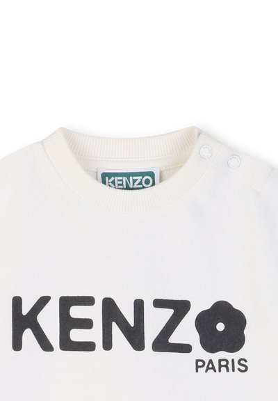 Witte katoenen trui met ronde hals, met zwarte teksten "KENZO" en "PARIS" en een bloemenlogo. Twee drukknoopjes op de linkerschouder.