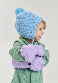 Blauer gestrickter Hut mit Pompon, strukturierte Muster, grüner Pullover und lavendelfarbene Handschuhe mit elastischen Bündchen, alles vor einem schlichten Hintergrund.