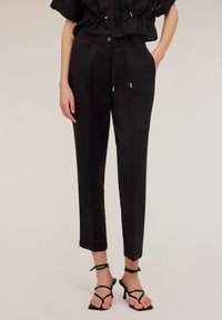 Zwarte op maat gemaakte broek met een rechte pijp, voorzien van een gladde textuur, voorzakken, knoopsluiting en omgeslagen zoom. Gepaarde met zwarte sandaaltjes.