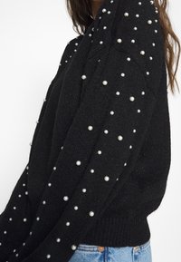 Pullover nero in maglia con un design testurizzato e decorazioni in perline bianche sulle spalle e sulle maniche. Vestibilità standard con polsini a costine.