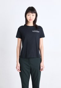 Zwarte katoenen t-shirt met korte mouwen, ronde hals en een witte grafische print op de borst. Gecombineerd met donkergrijze op maat gemaakte broek.