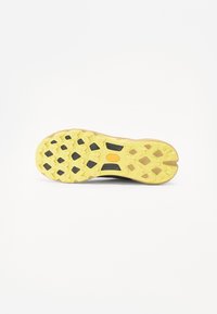 Black shoe sole with a zigzag pattern, featuring a yellow outer layer and a black rubber grip. Notable brand logo in orange.
