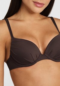 Reggiseno imbottito marrone con spalline regolabili, caratterizzato da una texture di tessuto liscia e un classico design a triangolo, che mette in risalto una silhouette elegante.