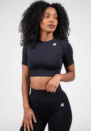 Zwarte sport crop top met korte mouwen, voorzien van een textuurpatroon, logo op de schouder en een gemerkte tailleband. Gepaarde met zwarte high-waisted leggings.