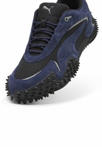 Sneaker in pelle scamosciata blu e reti nere con suola in gomma nera texturizzata che presenta sporgenze simili a spuntoni e un accento metallico.