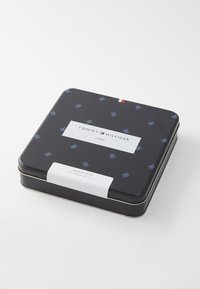 Schwarze rechteckige Dose mit einem sich wiederholenden blauen Logomuster, weißem Etikett mit Produktdetails und rotem Akzentstreifen oben.
