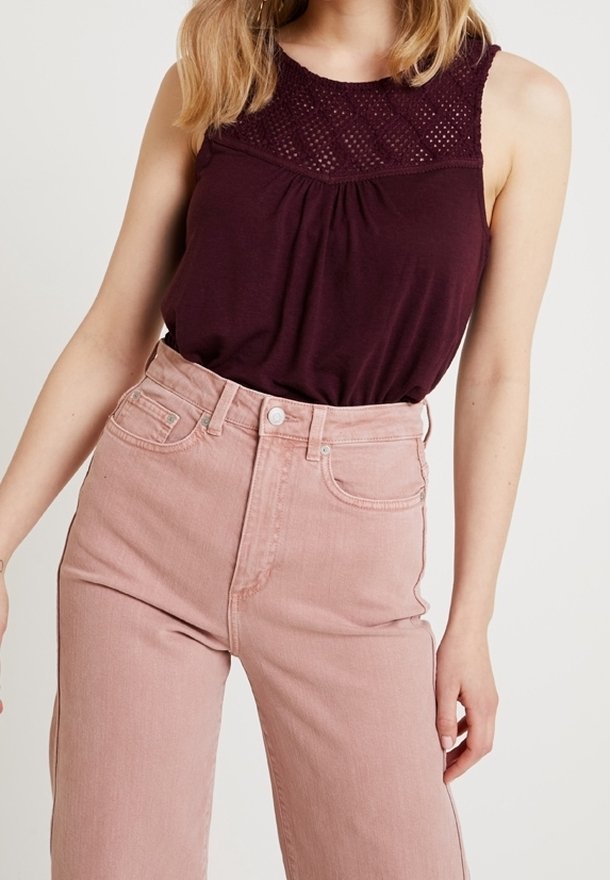 Burgundy ärmlös topp med texturerad halsringning, tillsammans med högmidjade rosa denimjeans. Toppen har en avslappnad passform och rynkdetaljer.