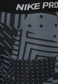 Legginsy Nike Pro z czarno-szarym geometrycznym wzorem, zawierające różne kształty i kropkowane motywy. Elastyczna talia z logo.