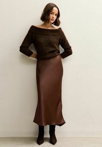Brown knitted off-shoulder sweater paired with a brown satin maxi skirt and knee-high brown boots, set against a neutral background.