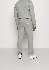 Man som bär grå Nike-träningsbyxor och matchande sweatshirt, står med ryggen mot kameran, vita Nike Air-sneakers synliga.
