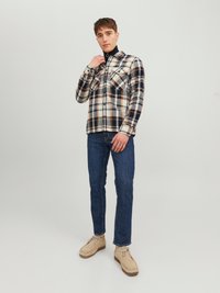 Camisa de franela a cuadros en beige, azul marino y marrón; con dos bolsillos en el pecho, botón frontal; combinada con jeans oscuros y botines desérticos beige.