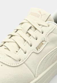 Witte suède sneakers met een getextureerd oppervlak, voorzien van platte veters, een goudkleurig logo op de tong en een subtiel zijstrependesign.