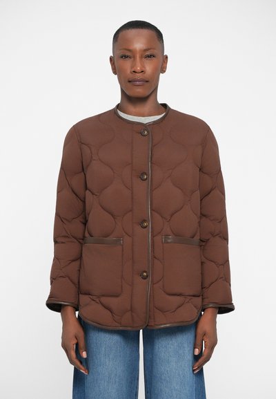 Braune gesteppte Jacke mit runden Mustern, vier Knöpfen und zwei vorderen Taschen. Akzentuiert mit braunen Besätzen, kombiniert mit weiten blauen Denim-Hosen.