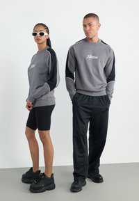 Grå hettegenser med svarte detaljer og hvit logo, kombinert med svarte shorts og kraftige sorte joggesko. Strukturlignende stoff, sporty design.