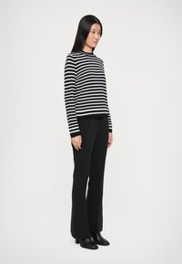 Maglione a righe bianco e nero in maglia, con maniche lunghe e scollatura rotonda, abbinato a pantaloni neri a zampa e stivali neri con tacco.