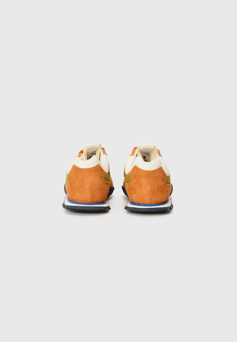Zapatillas con una mezcla de ante en naranja, verde y blanco. Presentan una forma redondeada y una suela texturizada con un acento azul en el talón.