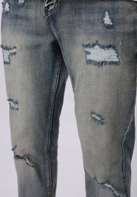 Hellblaue, ausgebleichte Jeans mit fransigen Nähten und unterschiedlichen Blautönen. Besitzt eine schlanke Passform und ein klassisches Fünf-Taschen-Design.