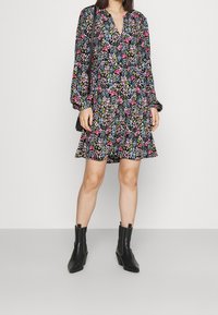 Kukkakuosisessa mekossa on musta tausta, pitkät hihat ja v-pääntie. Mekon kanssa on yhdistetty mustat korkokengät nilkkapituiset saappaat.