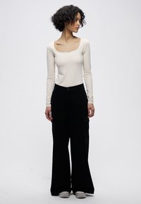 Hosszú ujjú, testhez simuló bézs felső laza, magas derekú fekete kordbársony nadrággal, melyen cargo zsebek találhatók. Semleges színű sportcipők alul.