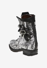 Bota de cuero veteado en blanco y negro, de altura hasta el tobillo, con acentos de doble hebilla, superficie texturizada y una suela negra resistente.