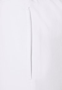 Tela blanca con una textura suave, con una costura vertical y sutiles detalles de costura. El diseño enfatiza la simplicidad y el minimalismo.