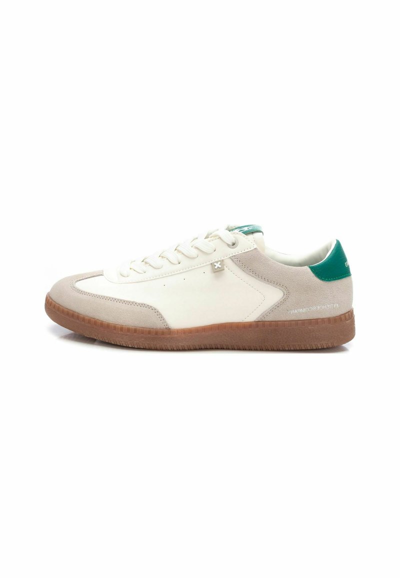 Zapatilla blanca y gris claro con un upper de gamuza texturizada y cuero liso. Presenta un detalle en el talón verde y una suela de goma marrón.