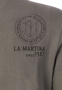 Gray sweatshirt featuring embroidered circular logo and text detailing "LA MARTINA since 1987" in dark thread. Soft fabric texture.