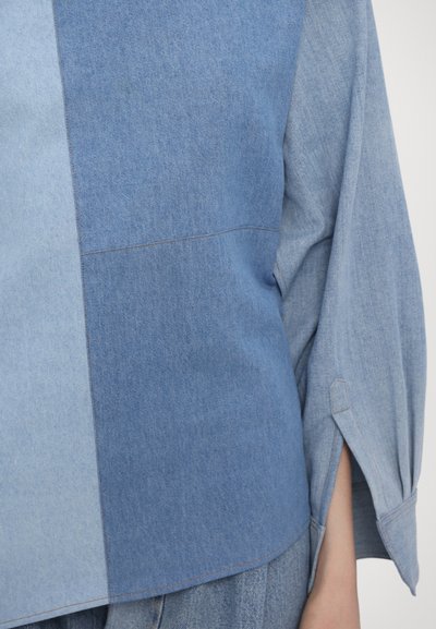 Denim shirt featuring varied shades of blue, a slight texture difference, wide sleeves, and side slits for design detail.