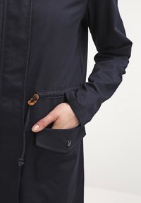 Marinblå, lätt jacka med texturerad yta, med en framficka med knäppning och justerbar dragsko vid midjan.