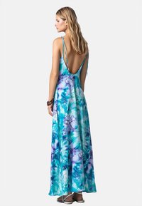 Abito lungo con schiena scoperta, caratterizzato da un motivo tie-dye blu e verde, con spalline sottili e una texture di tessuto fluente.