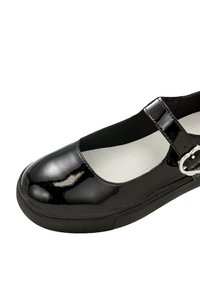 Czarne lakierowane buty typu mary jane z okrągłym noskiem, elastycznym paskiem i klamrą. Teksturowana czarna gumowa podeszwa. Biała wewnętrzna wyściółka.