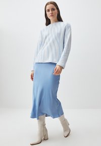 Maglione azzurro chiaro in pelliccia sintetica con strisce ondulate bianche, abbinato a una gonna in satin blu uniforme e stivali alti bianchi con tacco.