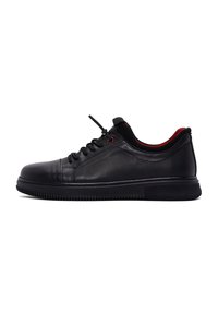 Scarpa atletica in pelle nera con design perforato, dettagli rossi, chiusura con lacci e suola in gomma spessa. Superficie strutturata per una migliore aderenza.